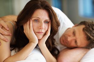 Sexual related problems - Middle aged woman lying on bed beside her husband in deep thought